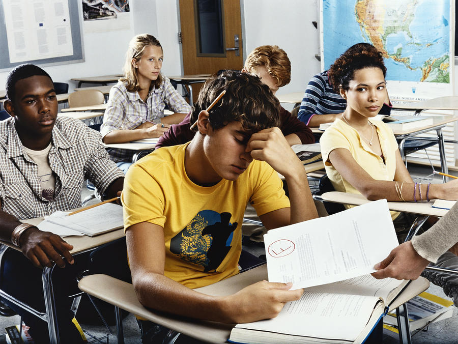 Teenage Boy Sits Looking Down in Embarrassment as he is Given a Failed Exam Paper Photograph by Digital Vision.