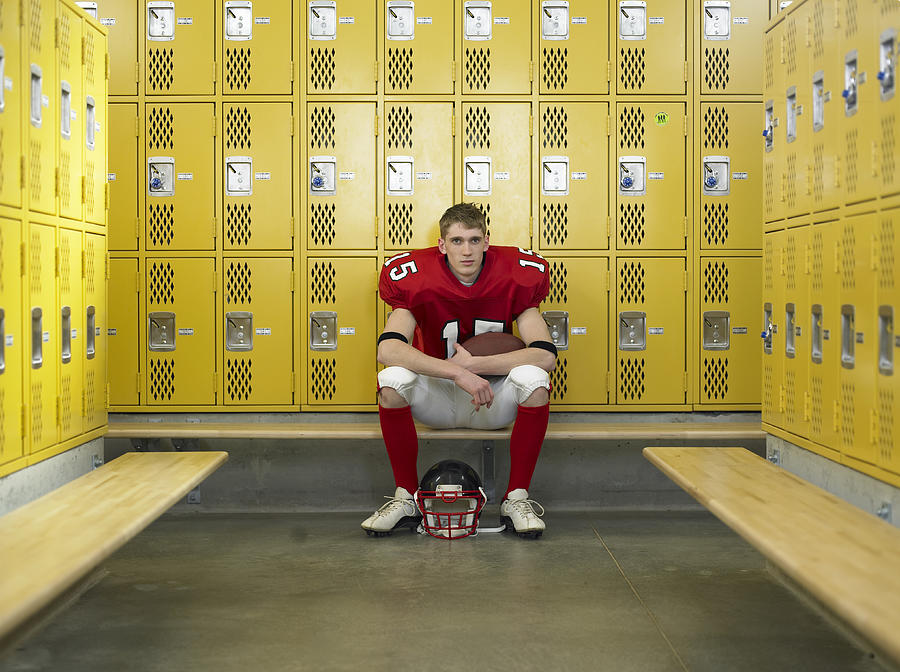 Teenage football player (15-17), sitting in locker room, portrait Photograph by Thomas Barwick