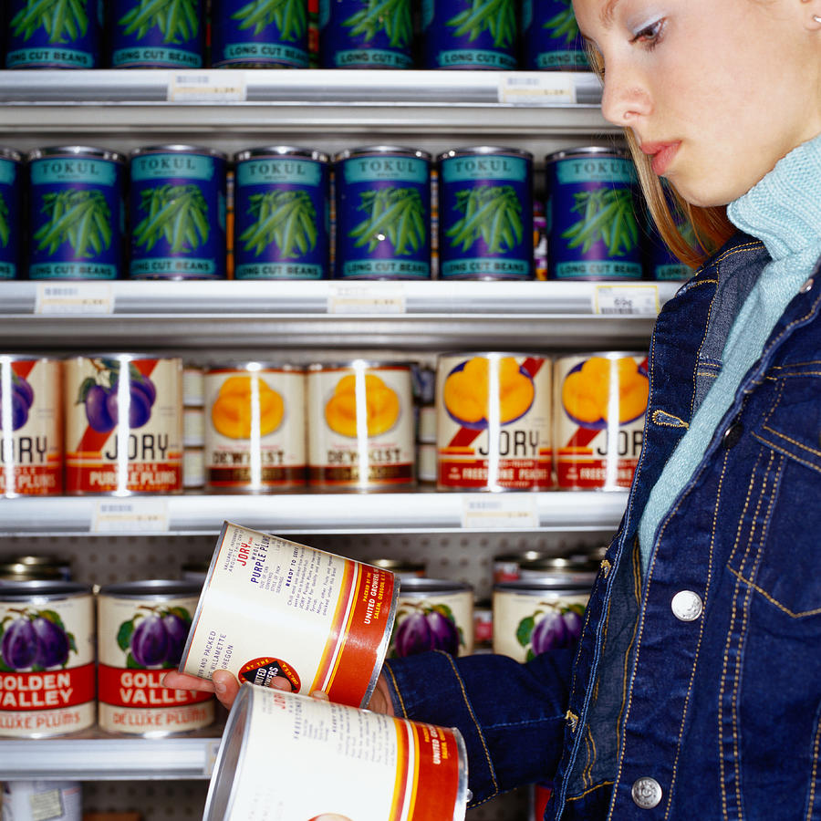 Teenage girl (14-16) looking at cans in supermarket, side view Photograph by Chad Baker/Jason Reed/Ryan McVay