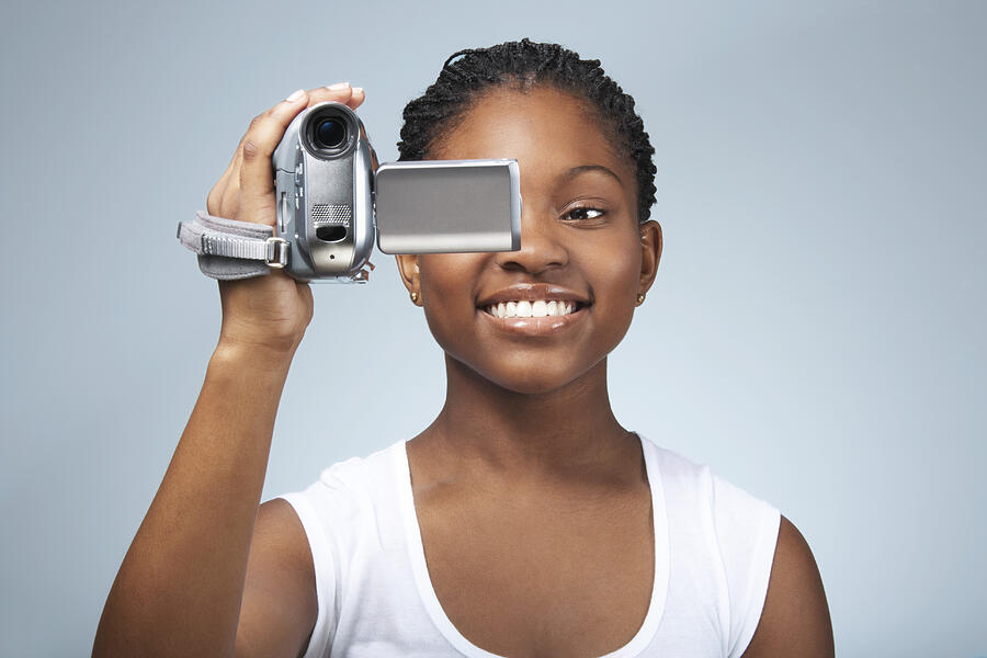 Teenage girl (15-17) using video camera, smiling, close-up Photograph by James Woodson