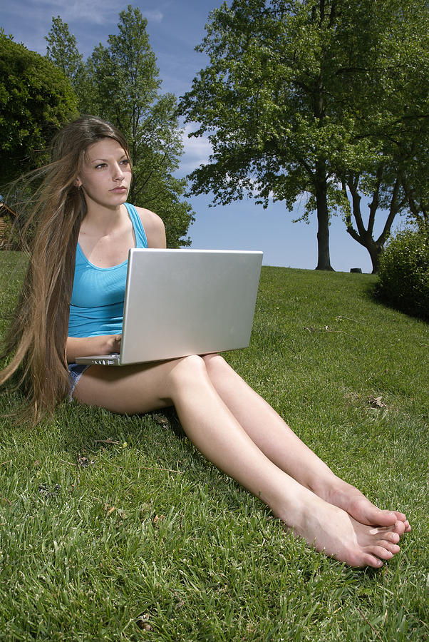 Teenage girl (16-17) sitting on grass and using laptop Photograph by Paul Hanson