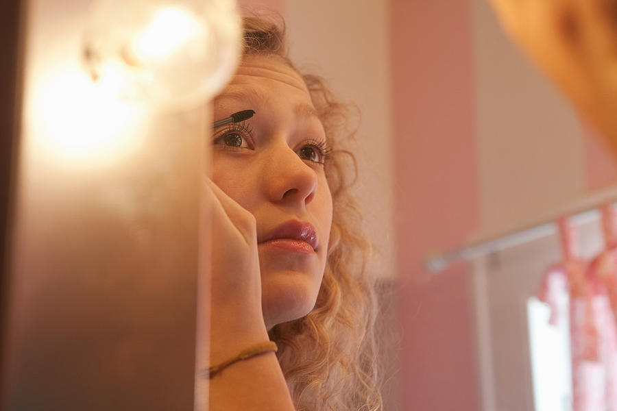Teenage girl applying mascara in mirror Photograph by Image Source