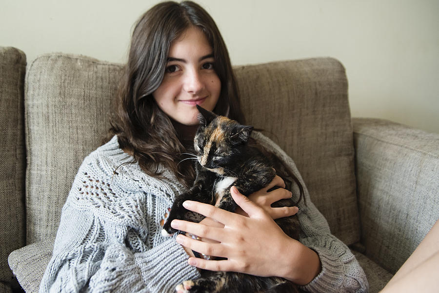 Teenage girl cuddling kitten on living room sofa. Photograph by Martinedoucet