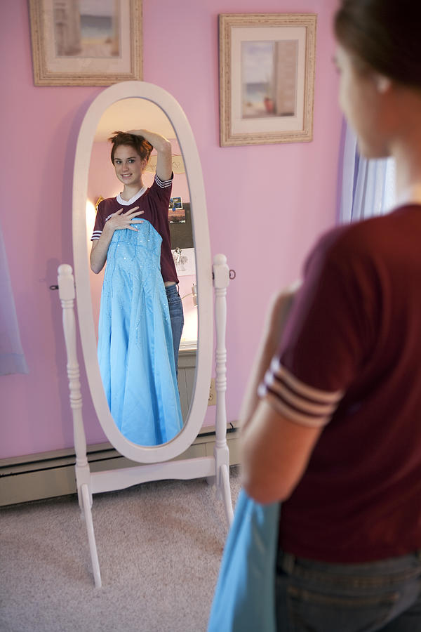 Teenage girl holding dress in front of mirror. Photograph by Andreas Kuehn