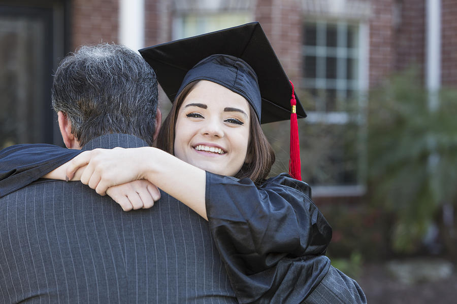 Teenage girl hugging father at graduation Photograph by Kali9