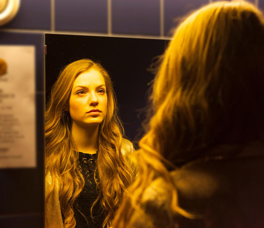 Teenage girl looking at her reflection in mirror Photograph by Henglein and Steets