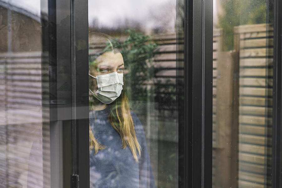 Teenage girl looking through window with mask Photograph by Justin Paget