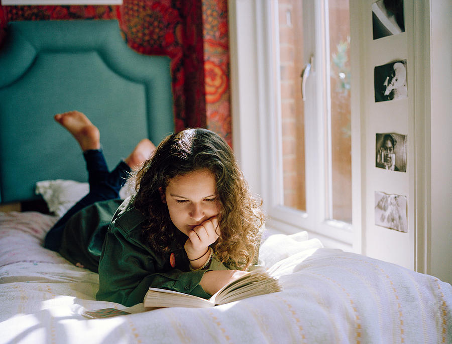 Teenage Girl Lying On Her Bed, Reading A Book Photograph by Alys Tomlinson