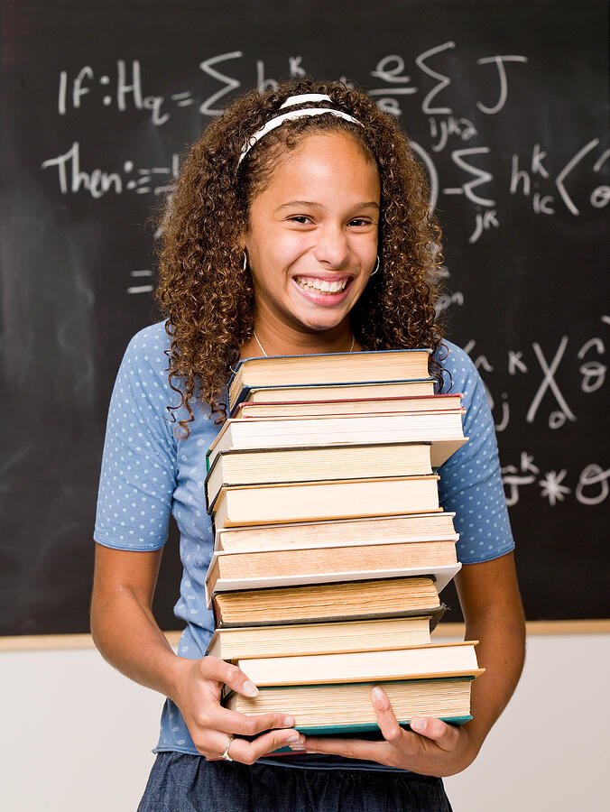 Teenage girl student posing in classroom with stack of books Photograph by Jupiterimages