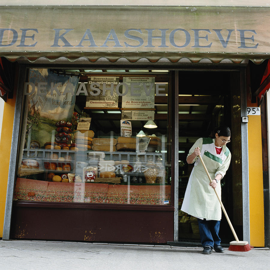 Teenage Girl Sweeping Outside of a Delicatessen Photograph by Ryan McVay