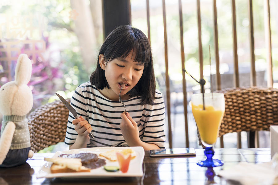 Teenage girl using smartphone in the restaurant Photograph by Owngarden