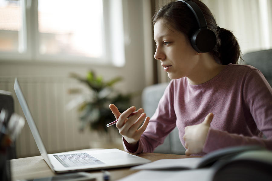 Teenage girl with headphones having online school class at home Photograph by Damircudic