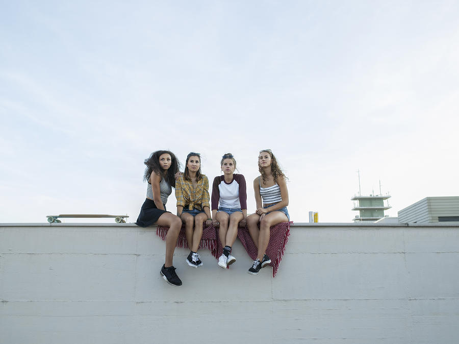 Teenage girls sitting on rooftop wall Photograph by Joos Mind