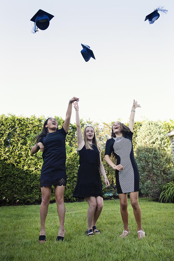 Teenage girls throwing graduation hats in backyard. Photograph by Martinedoucet