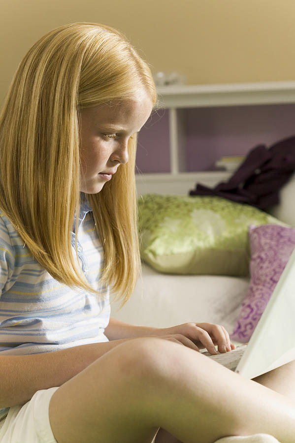 Teenage Lifestyle Shot Of A Blonde Female As She Sits On Her Bed Using Her Laptop Computer Photograph by Photodisc