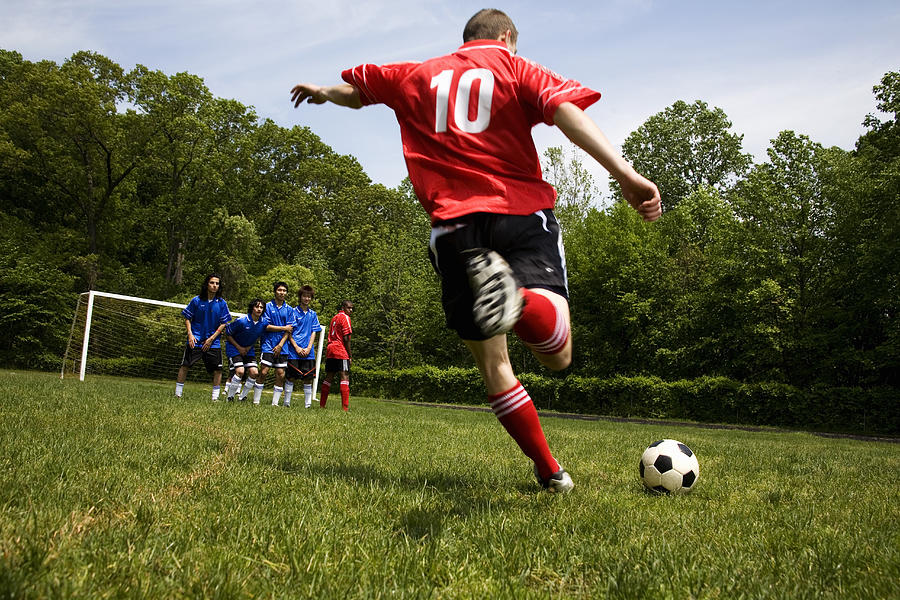 Teenage male (18-20) soccer player free kicking against opposing team Photograph by Rana Faure
