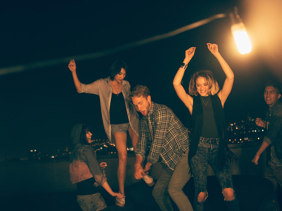 Teenager friends dancing and laughing on a rooftop party Photograph by Wundervisuals