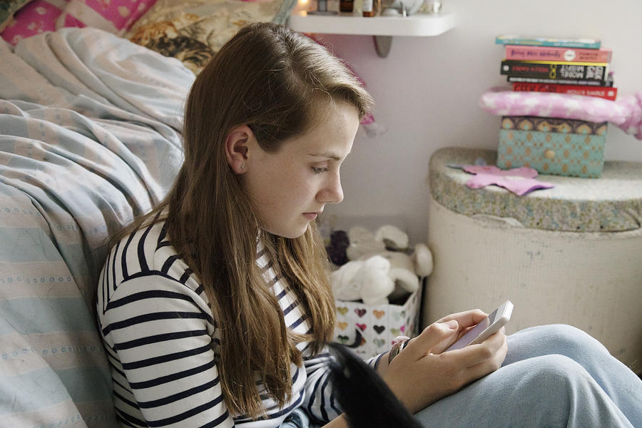 Teenager sitting in her bedroom, texting on mobile phone. Photograph by Betsie Van Der Meer