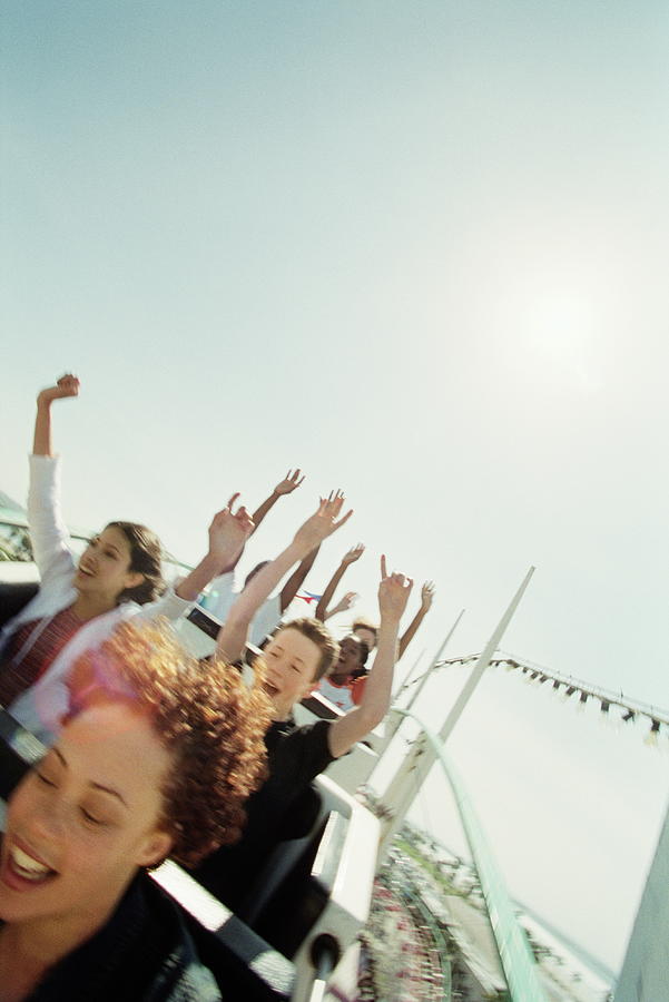 Teenagers (14-18) riding   rollercoaster, hands raised in air Photograph by Joe McBride
