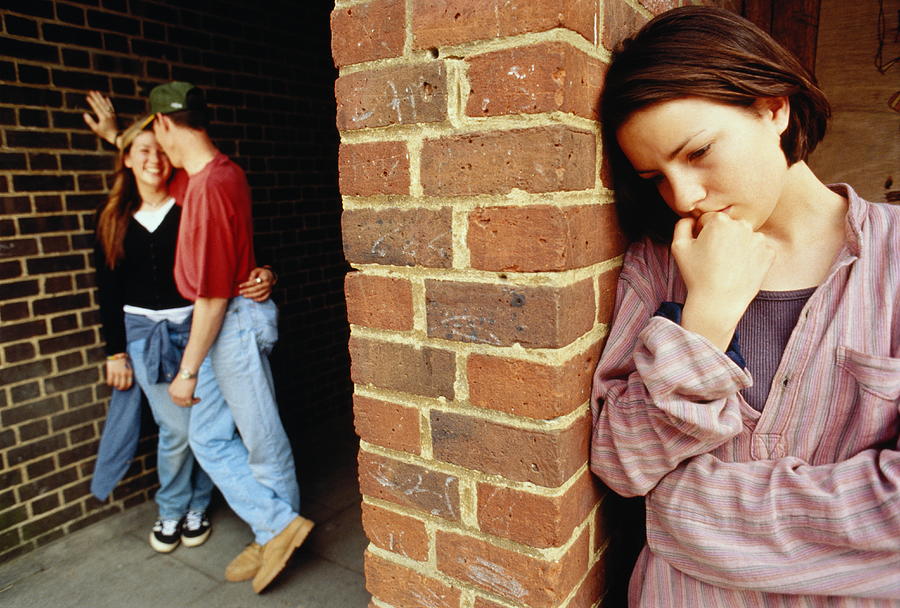 Teenagers (15-17), girl with sad expression, couple in background Photograph by Penny Tweedie