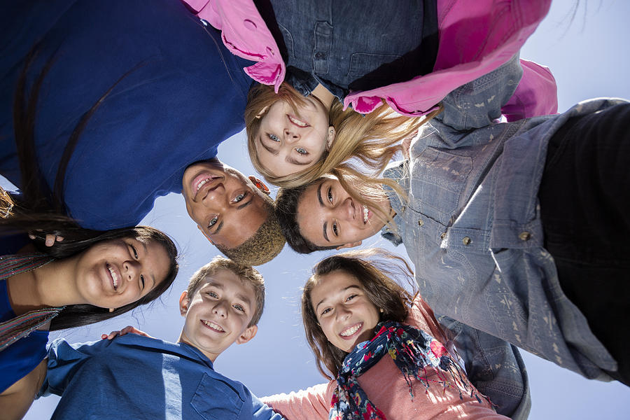 Teenagers: Multi-ethnic group of friends huddle outside together. Blue sky. Photograph by Fstop123