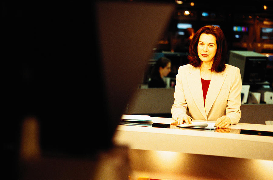 Television anchorwoman sitting at desk smiling at camera Photograph by Ryan McVay
