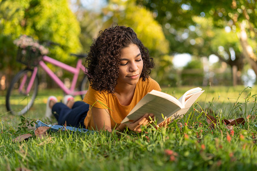 Tenn girl reading a book lying on the grass Photograph by MesquitaFMS