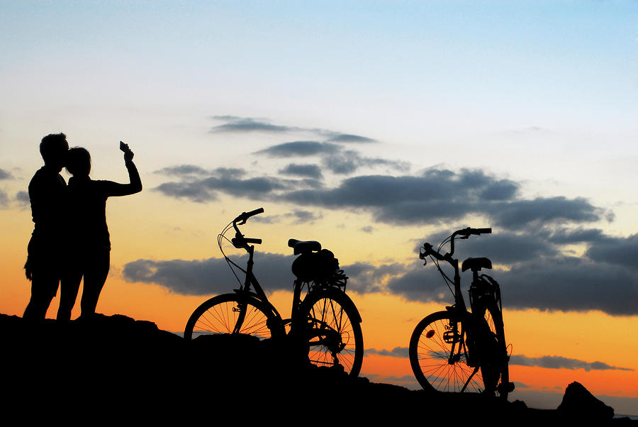 The couple doing  selfie on the sunset with bikes in sunset Photograph by Severija Kirilovaite