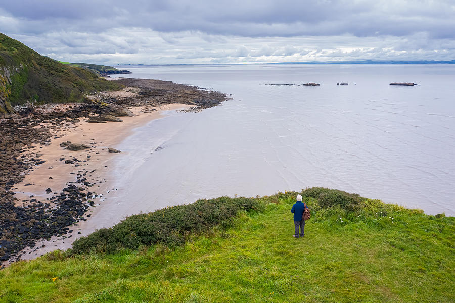 The drone view of a senior man standing alone at the coast in Dumfries and Galloway, south west Scotland Photograph by JohnFScott