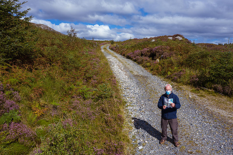 The high angle view of an active senior man wearing a face mask while standing on a dirt road in a remote part of Dumfries and Galloway, south west Scotland Photograph by JohnFScott