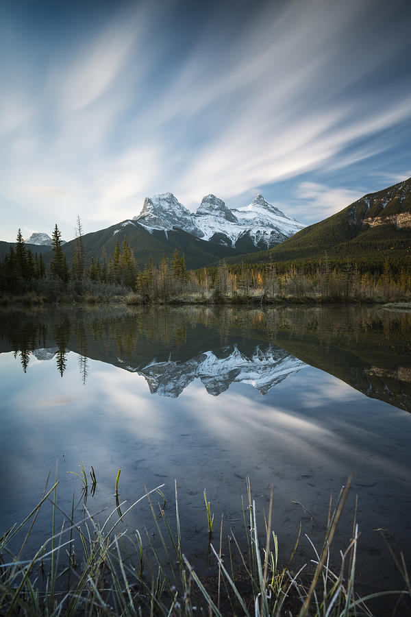 The iconic three sisters mountains reflected in a still pool, Canmore, Alberta, Canada Photograph by Nick Fitzhardinge