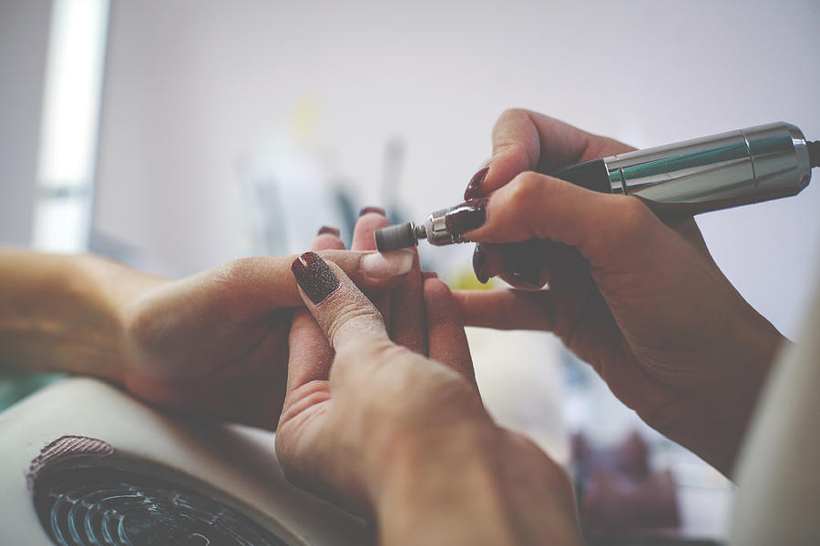The process of manicure at a beauty salon with electrical  file.  Close up. Photograph by Liderina