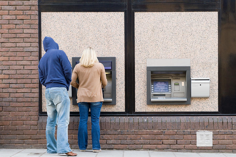 Thief looking over womans shoulder at cash machine Photograph by Image Source