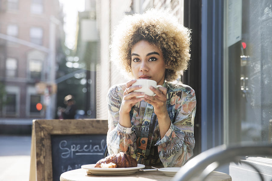 Thoughtful woman holding coffee cup while sitting at sidewalk cafe Photograph by Cavan Images
