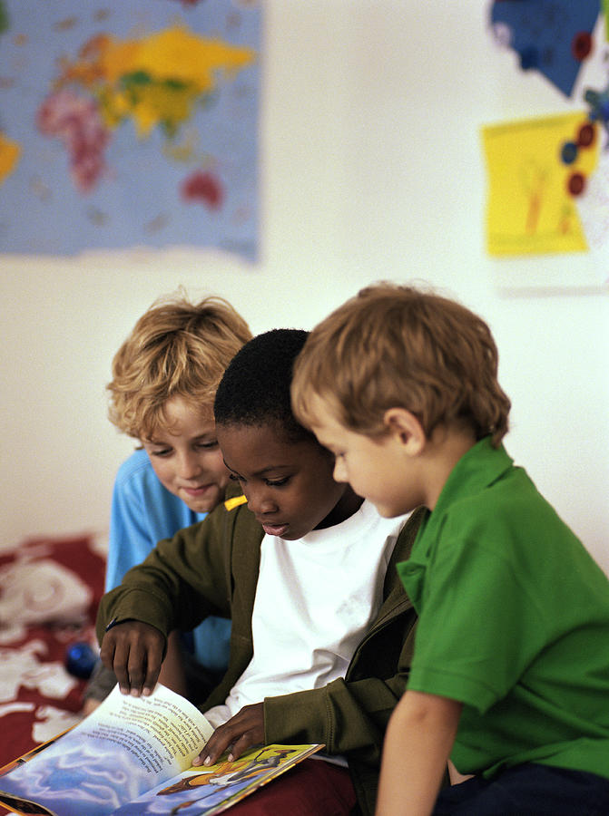 Three boys (6-8) looking at book together Photograph by Nick White