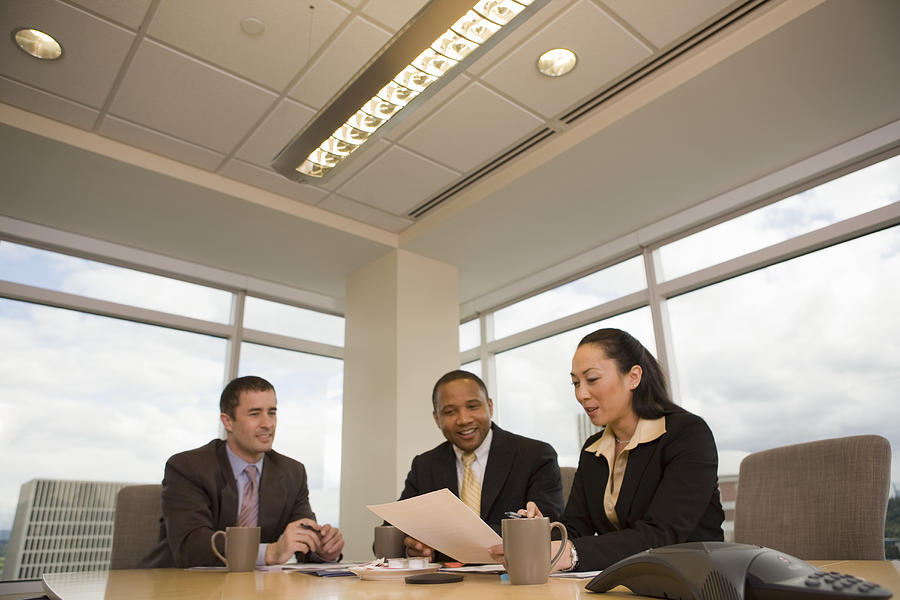 Three businesspeople looking at documents in conference room, smiling Photograph by John Giustina