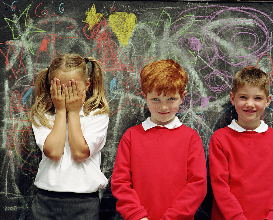 Three children (6-8) standing by blackboard, girl covering face Photograph by Digital Vision