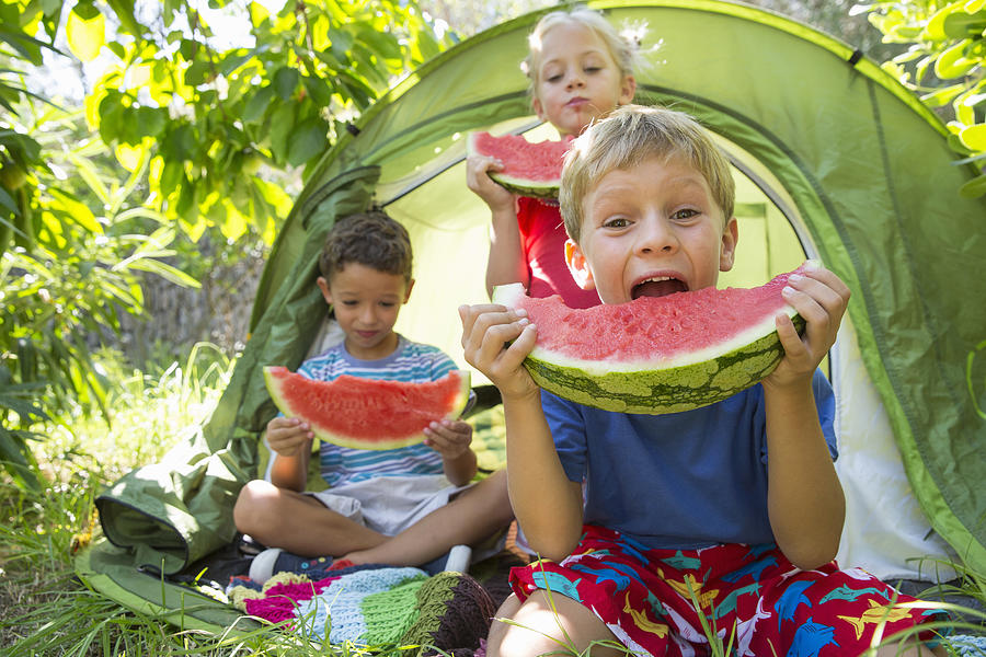 Three children eating large watermelon slices in garden tent Photograph by Russ Rohde