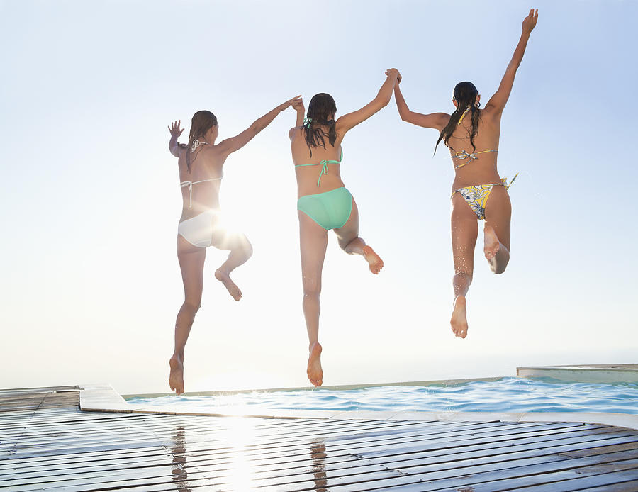 Three female friends jumping in swimming pool Photograph by OJO Images