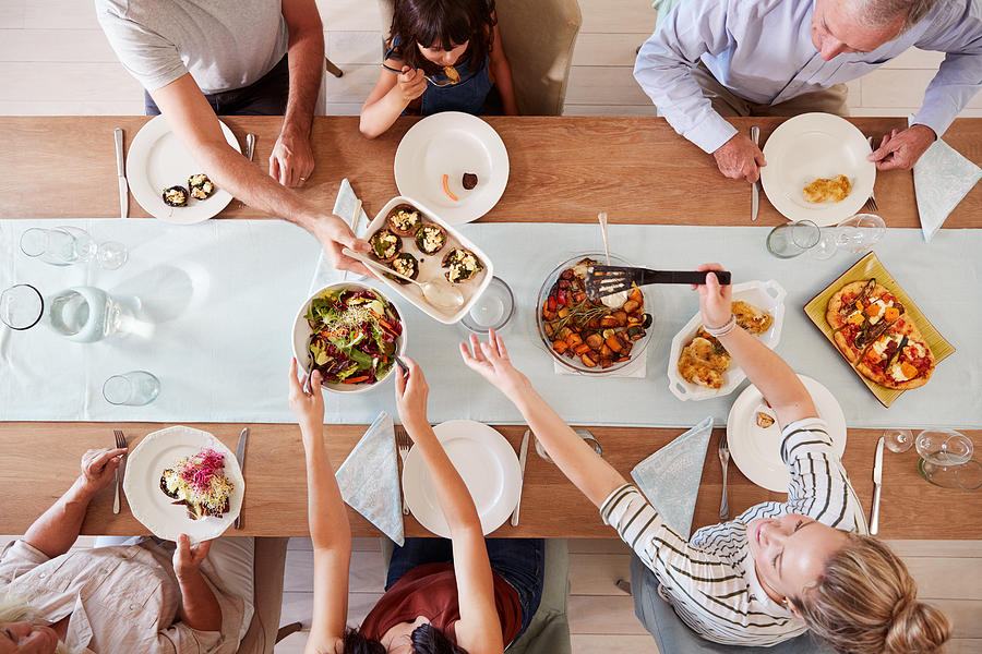 Three generation white family sitting at a dinner table together serving a meal, overhead view Photograph by Monkeybusinessimages