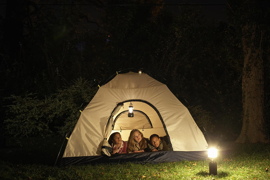 Three girls (10-11, 12-13) lying in tent in garden at night Photograph by Christopher Robbins