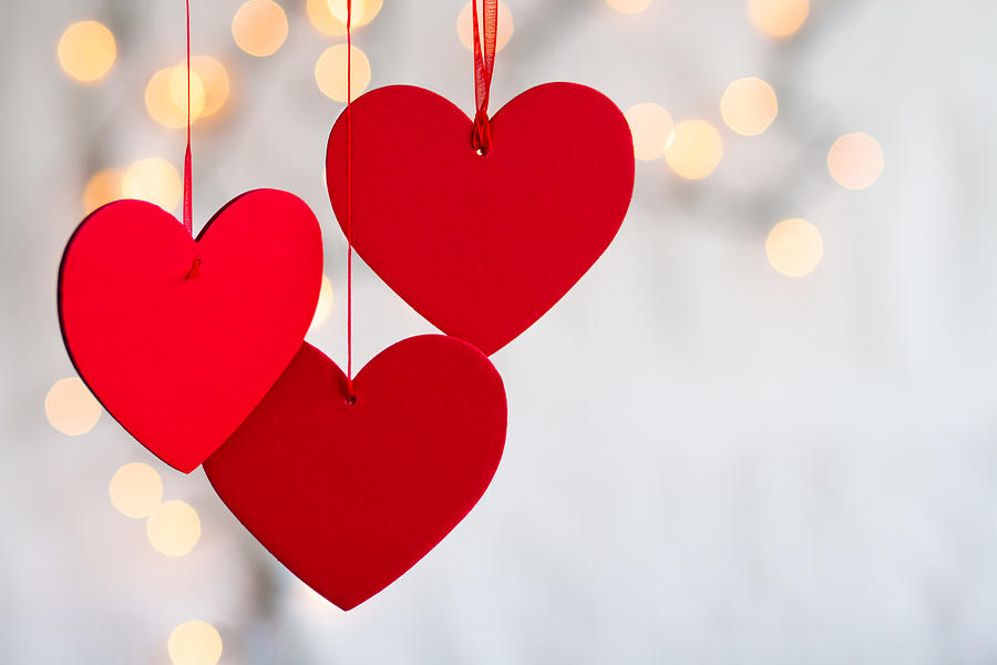 Three hanging red hearts on defocused light background. Photograph by Zianlob
