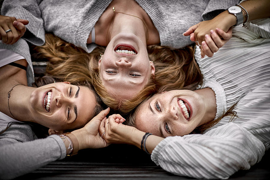 Three happy young women lying on a bench holding hands Photograph by Oliver Rossi