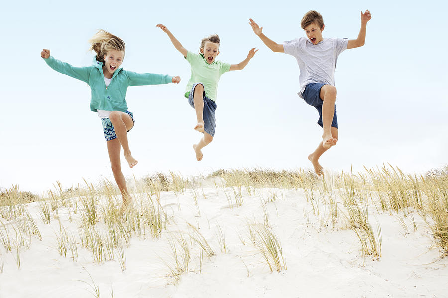 Three kids running and jumping off a sand dune. Photograph by Kristina Lindberg
