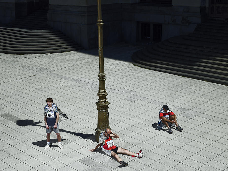 Three marathon runners wrapped in blankets relaxing on pavement Photograph by Michael Blann