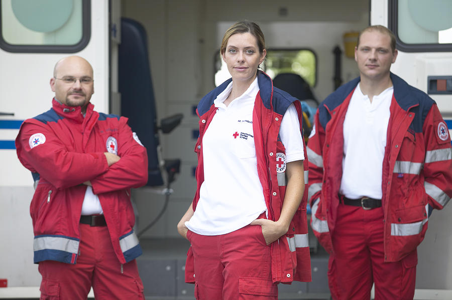 Three paramedics standing beside ambulance, portrait Photograph by Jochen Sand