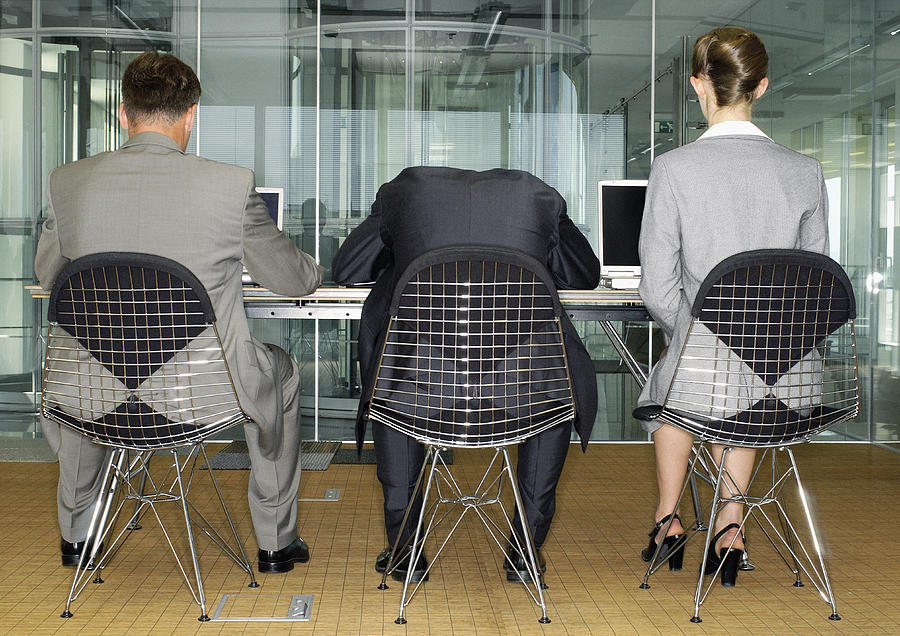 Three people in suits, using laptops, one has head on table, rear view. Photograph by Teo Lannie