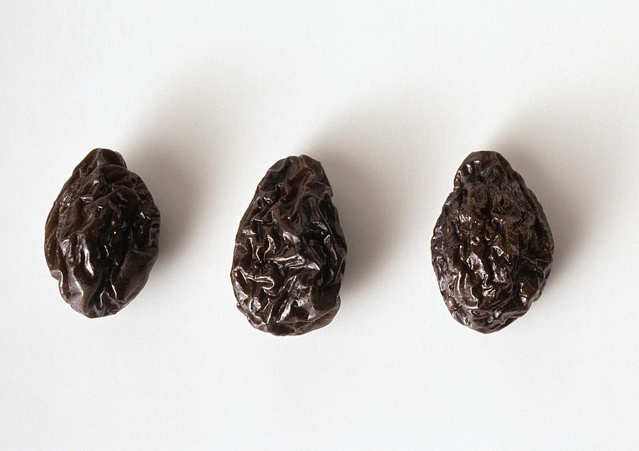 Three prunes against white background, close-up Photograph by Isabelle Rozenbaum & Frederic Cirou