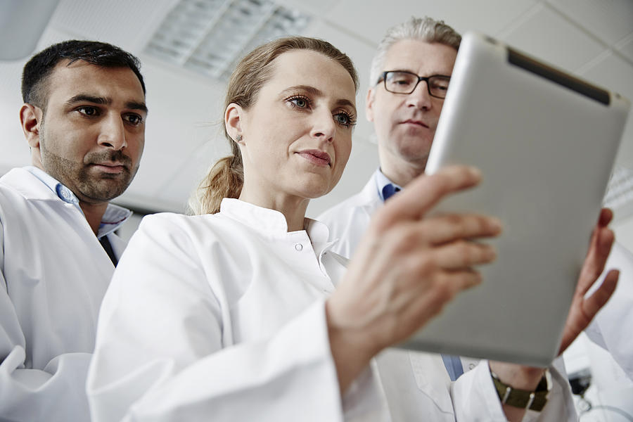 Three scientists in a laboratory, using tablet Photograph by Solskin