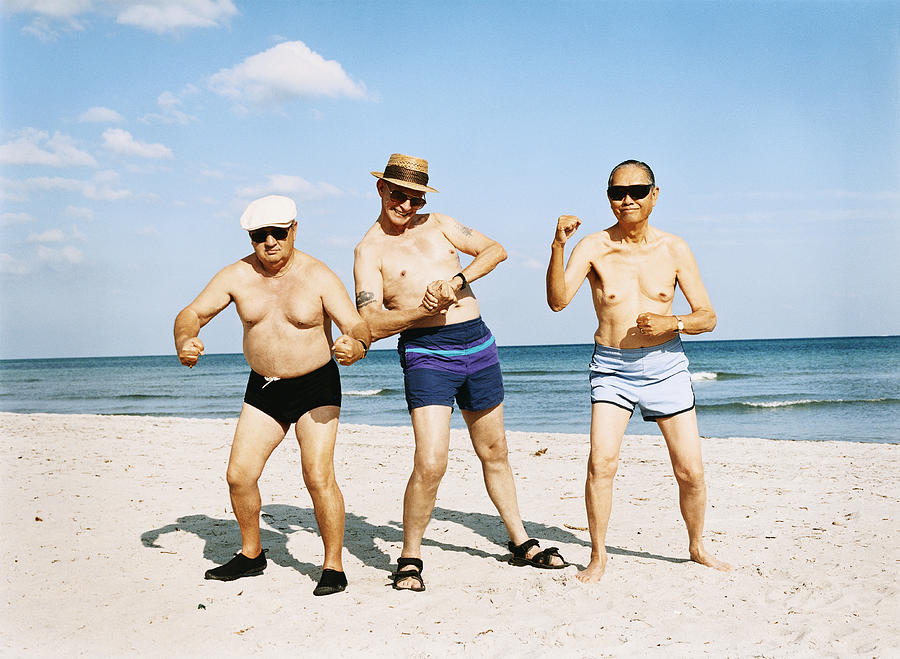 Three Senior Men in Swimming Trunks Stand on the Beach Flexing Their Muscles Photograph by Digital Vision.